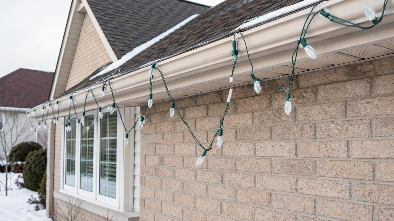 Close-up of sagging temporary Christmas light wires and loose clips attached to a home's gutter and soffit.