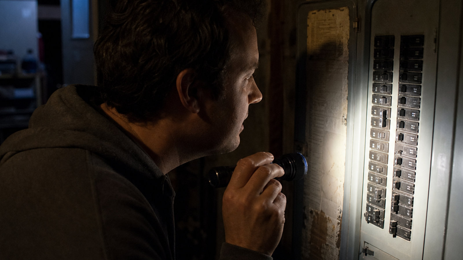 eowner shining a flashlight on an electrical circuit breaker panel in the dark to check for a partial house power outage.