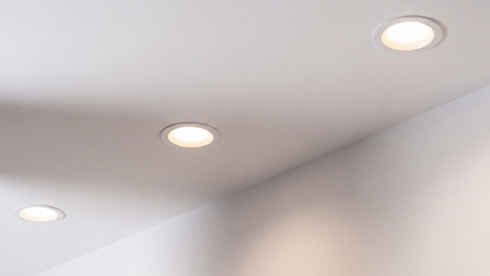 Close-up of evenly spaced, flush-mounted LED pot lights glowing on a modern white drywall ceiling.